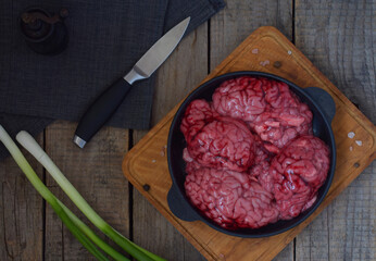 Beef brain shown on rustic wood in soft daylight. Close-up perspective emphasizing the brain’s...