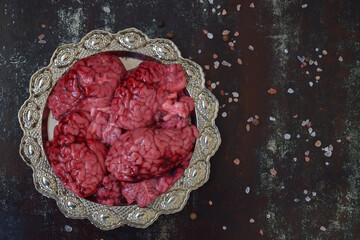 Beef brains arranged on ornate metal plate surrounded by salt grains over black textured surface...