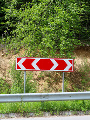 A bright red-and-white chevron sign stands by the road, signaling a sharp curve. In the background,...