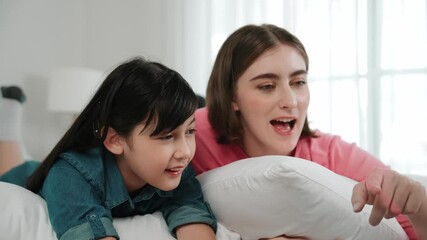 Attractive daughter and caucasian mother watching movie at laptop screen while lie on bad. Happy family spend time together before bed time. Parent and cute girl enjoy playing games together Pedagogy. - Powered by Adobe