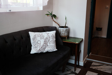 Vintage dark sofa with a peacock-embroidered pillow next to a potted plant. Cozy and traditional interior corner with handmade decor