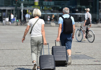 Man and woman walking to the train station with suitcases as cyclist passes by

