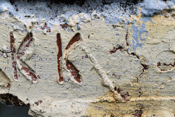 Carved initials in weathered concrete surface with peeling paint texture