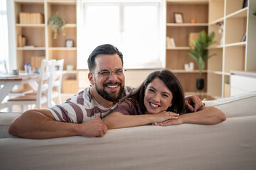 Happy couple smiling and leaning on sofa back at home