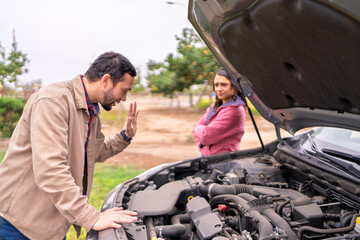 Frustrated couple checking broken down car engine on roadside