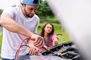 Mechanic connecting jumper cables to car battery for breakdown assistance