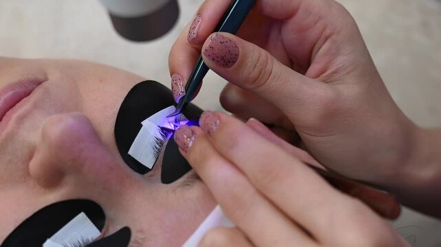 A woman undergoing eye lash extension procedure using an ultraviolet lamp.