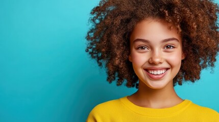 A cheerful young girl with curly hair and a bright yellow sweater beams with joy, embodying happiness and exuberance against a vibrant turquoise backdrop.