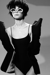 stylish woman wearing black bodysuit and oversized jacket with white sunglasses, short dark hair,...