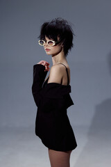 stylish woman wearing white sunglasses and a black off-shoulder dress posing with short dark hair...