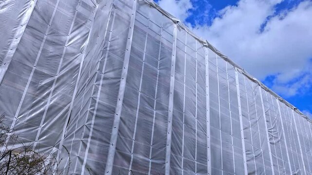 Building renovation scene. Story house covered with protection and scaffolding wrap plastic to waterproof the project. 