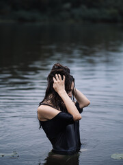 Beautiful long-haired brunette swims in the river in cloudy weather