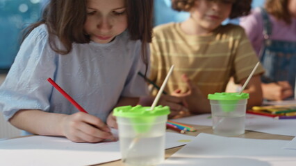 Artclass girl drawing pencil sitting table with classmates engaged work closeup.