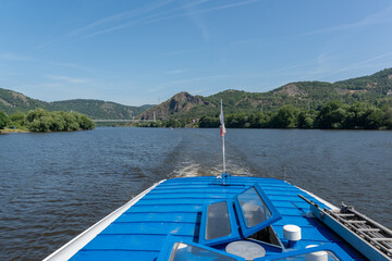 A picturesque scene from a boat showcasing tranquil waters, rolling hills, and vibrant greenery,...