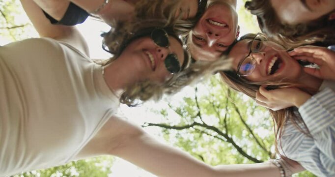 A group of carefree friends looking down at the camera, laughing and coming together in a joyful huddle. Their bond and happiness are evident in this bright summer scene.