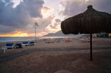 Relaxing Beach Scene at Sunset with Empty Chairs and Thatched Umbrella