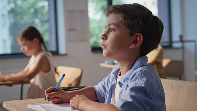 Cute schoolboy studying class writing in copybook at desk closeup. Little boy