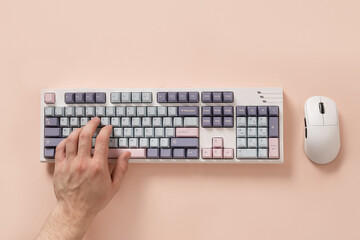 Mans hand texting and typing on modern mechanical keyboard and mouse on pink desk as background....