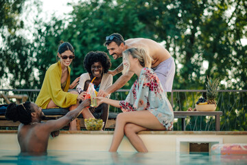 Naklejka na ściany i meble Friends toasting drinks at the poolside during summer vacation