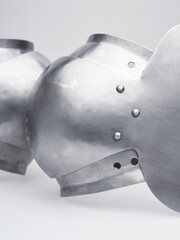 Close-up of medieval steel armor details with rivets and curved metal plates under soft light.
