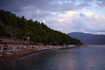 Fototapeta premium Serene Beachfront Overlooking Forested Hills Under a Dramatic Cloudy Sky