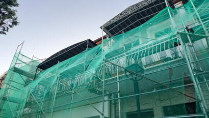 Facade of a building under renovation with green mesh scaffolding and balconies, concept of construction and urban development