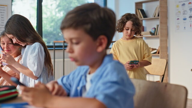 Focused schoolboy using smartphone in classroom lesson closeup. School children - Powered by Adobe