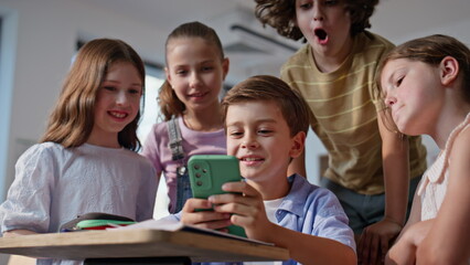 Excited schoolchildren playing mobile phone having fun together in class closeup