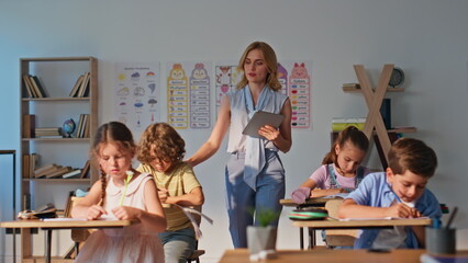 Group children doing homework sitting class desks. Young woman teacher watching 