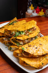 Stack of Mexican quesabirria tacos served on a white plate with sauces in the background