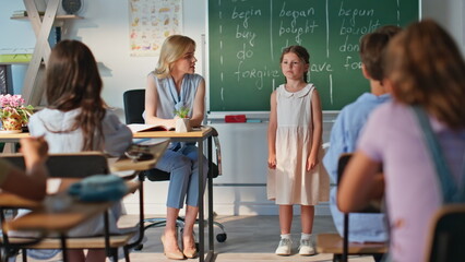 Educator listening schoolgirl speaking at classroom blackboard. Woman teacher