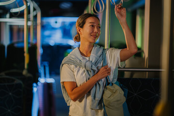 Asian woman holding handrail on moving bus at night