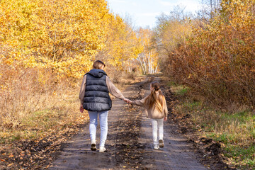 Fototapeta premium Rear view mother walking and holding hands with daughter for bonding, outdoor adventure or journey in nature. Mom strolling with child, kid or little girl on sidewalk in autumn season at park