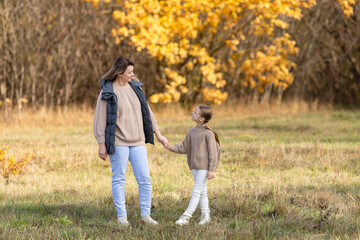 Mother and daughter walking holding hands at park. They are wearing warm clothes, main colors are...