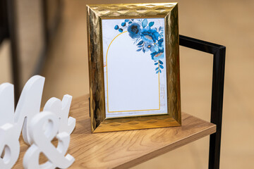 Golden picture frame with floral design on wooden shelf for wedding decoration