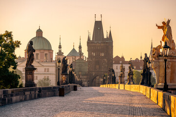Sunrise casts a warm glow over Charles Bridge in Prague, highlighting the statues and the historic...