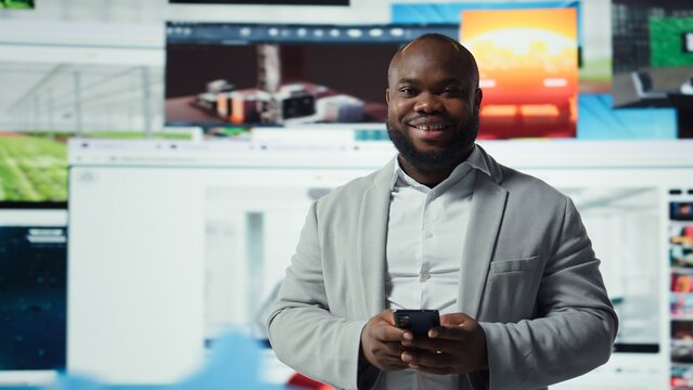 Portrait of cheerful man browsing social media feed on smartphone in front of digital video wall. Happy person using mobile phone, floating icons highlight interactive engagement online, camera A - Powered by Adobe