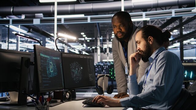 Supervisor in server room monitoring worker managing AI training datasets. African american team leader and engineer in data center supervising system operations supporting neural networks, camera A