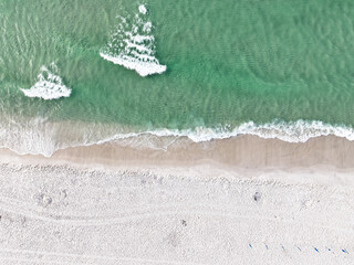 Bird's eye view of ocean waves crashing into a sandy beach in Pensacola, Florida