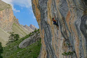Fearless female climber with intense focus ascends a beautifully textured rock face. She is searching for the next hold while climbing the steep cliff with rugged mountain scenery in the background.