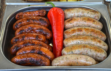 Delicious grilled sausages, arranged alongside bright red pepper, displayed in stainless steel...