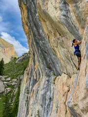 Fototapeta premium LOW ANGLE VIEW: Intensely concentrated climber works her way up a steep mountain face. Magnificent alpine environment with impressive rock formations is the perfect playground for adrenaline sports.