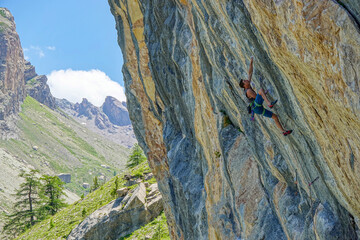 Male climber climbing a colourful, layered rock face, reaching for next hold. Outdoor climbing in...
