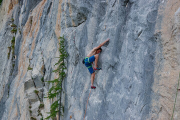 CLOSE UP: Shirtless male climber with immense strength and focus, grips a small hold on a steep,...