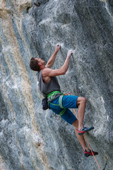 CLOSE UP, LOW ANGLE VIEW: Concentrated climber during ascend on a vertical rock face, with his hands gripping holds and legs providing balance. He is gazing upwards and he is looking for next grip.