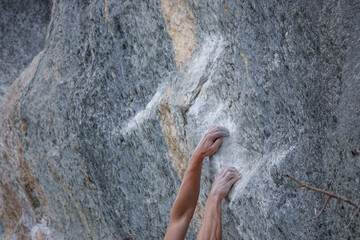 CLOSE UP: Hands, covered in white chalk, cling tightly to the textured surface of rock face....