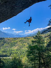 SILHOUETTE: Belayed climber hangs from a rocky overhang with an expansive mountain valley and a...