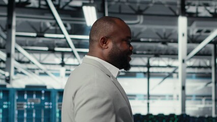 Happy businessman walking in data center, assessing rackmounts capacity before investing. Jolly management executive overseeing server farm built for business storage gear, camera B