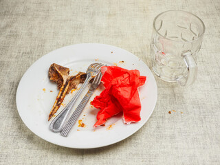 Finished high quality meal. Empty dirty plate with t bone, fork, knife and red napkin on white table cloth. Fine dinner concept. Scraps on a plate.