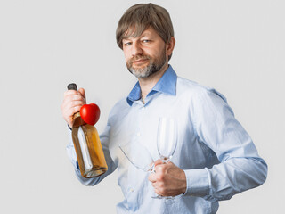 Man in his 50s in light color shirt is holding a bottle of sparkling wine with red heart. Romance and love concept. Male with grey short beard and slim muscular body type. Flirt and date theme.